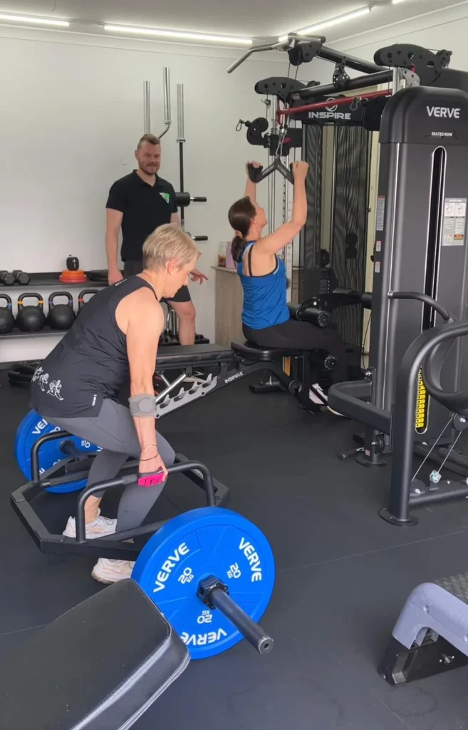 Two clients training in gym with personal trainer